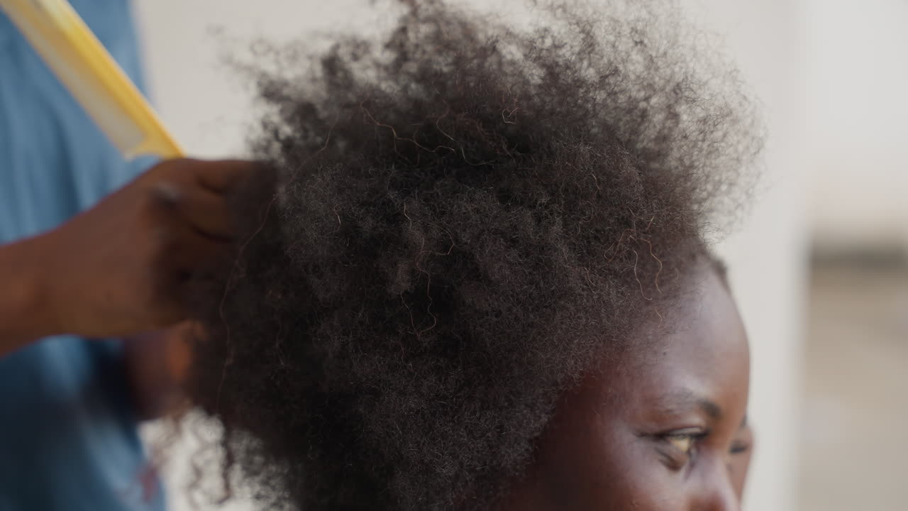 Primo piano di una donna che si prende cura dei ricci testurizzati. Donna nera che pettina delicatamente i capelli naturali e spessi con cura. Primo piano dettagliato di una stilista che gestisce con delicatezza i capelli afro testurizzati e le scaglie del cuoio capelluto.