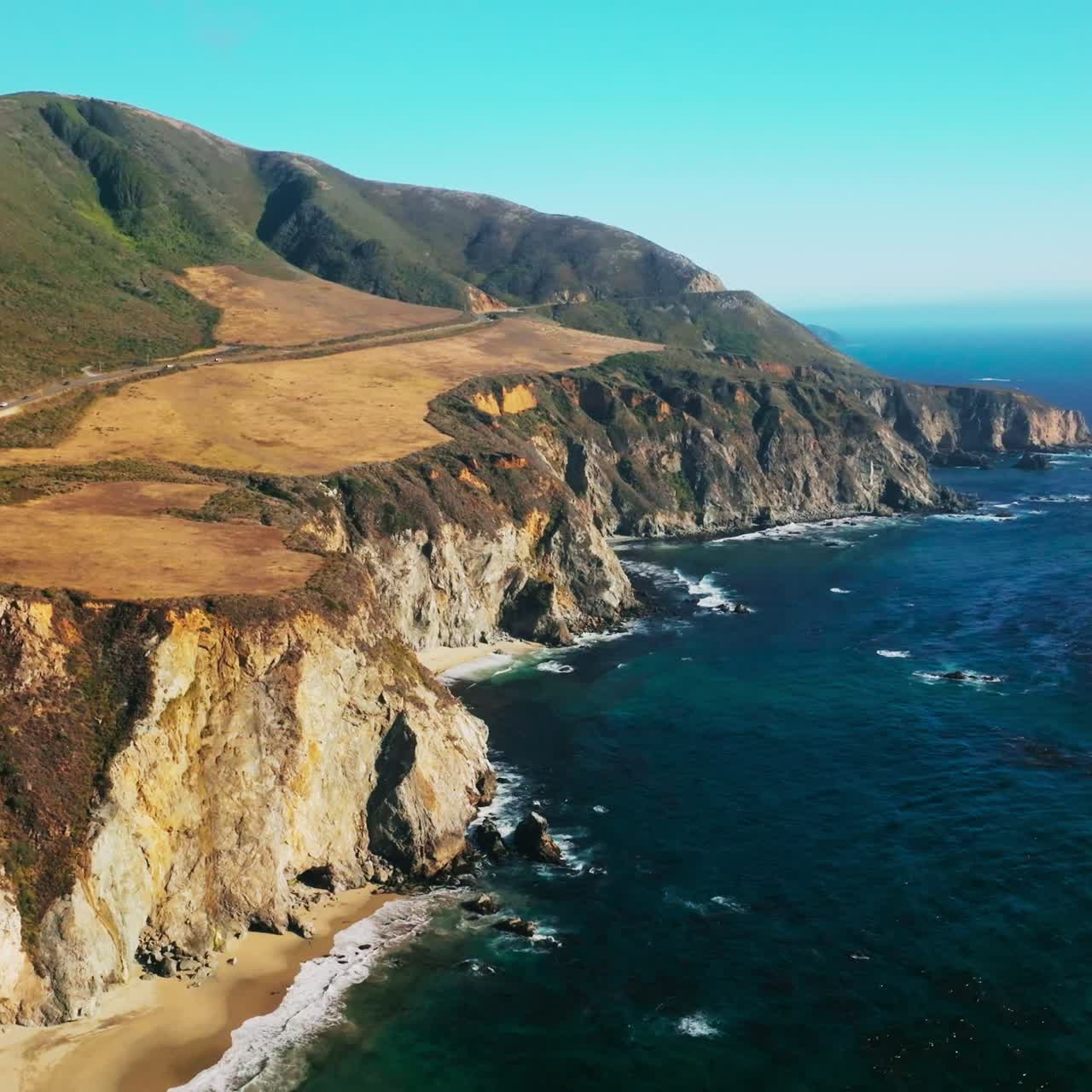 Pacific Ocean splashing waves by the steep cliff rocks. Amazing scenery of highways across the beautiful mountains. Blue skies at backdrop