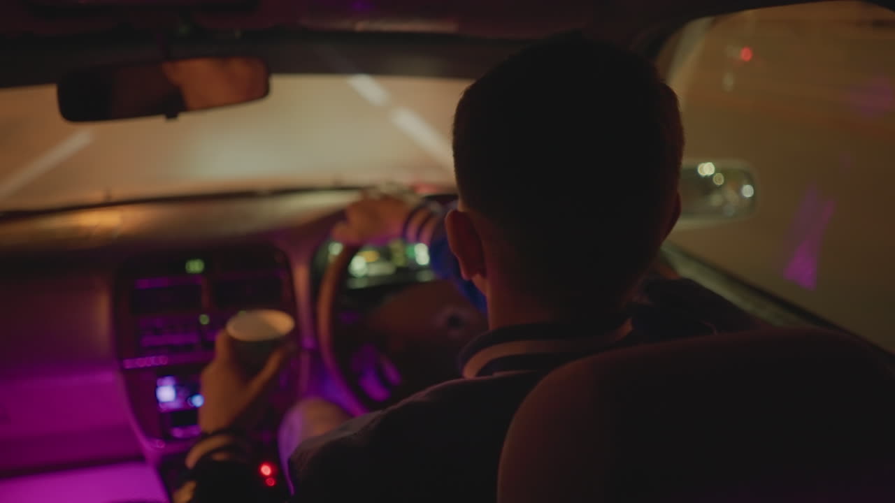 Un conductor consulta el teléfono móvil entre el brillo de las luces de neón mientras conduce tranquilamente por la ciudad. Un tranquilo interior de coche nocturno con luces de neón y un conductor que consulta su smartphone mientras conduce por las silenciosas calles de la ciudad.