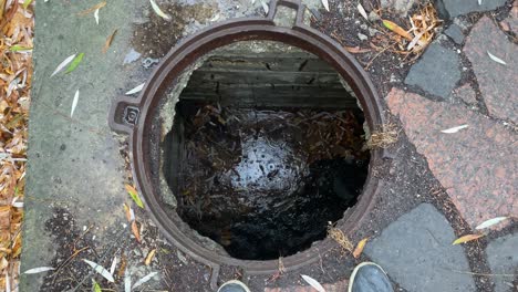 looking down into an open manhole showing sewer with waste water.