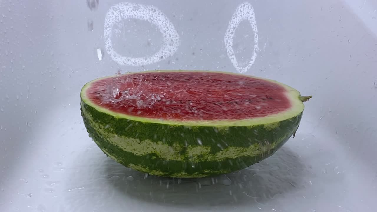 물의 제트가 잔한 은 익은 수박에 떨어지고 반으로 잘라서 스프레이를 떨어뜨립니다.