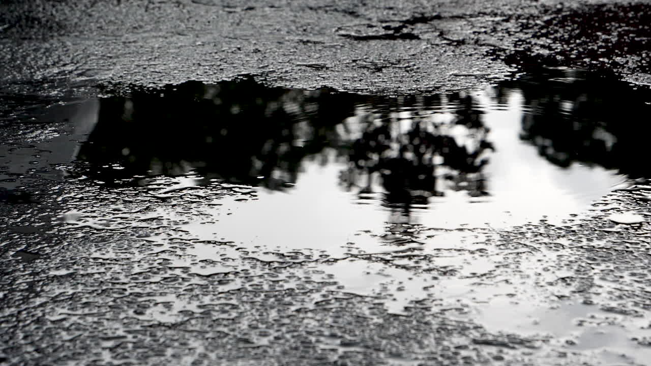 On a dark afternoon a light rain drops disturbs the mirror like puddle in a a lonely parking lot