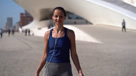 sporty girl in earphones smiling at camera on street