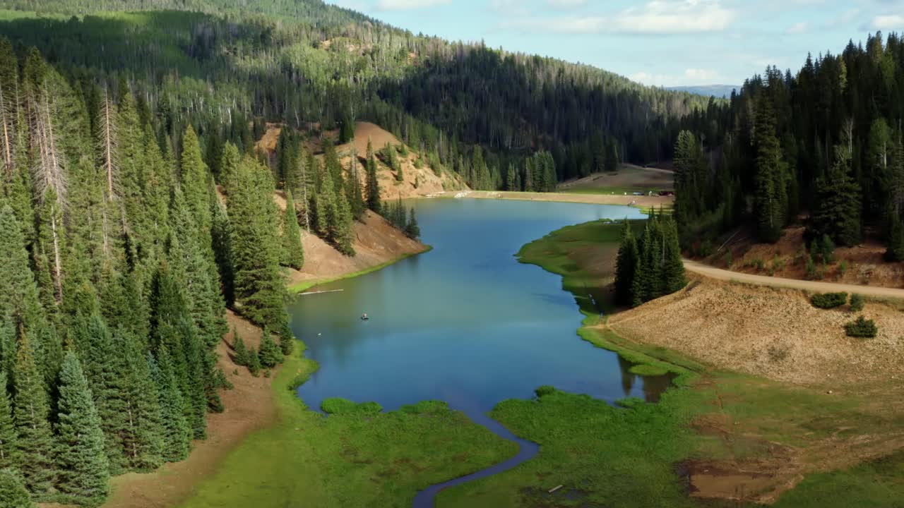 Beautiful ascending aerial drone shot of a stunning nature landscape of the Anderson Meadow Reservoir lake up Beaver Canyon in Utah with large pine tree forest, a small stream, and a grass field