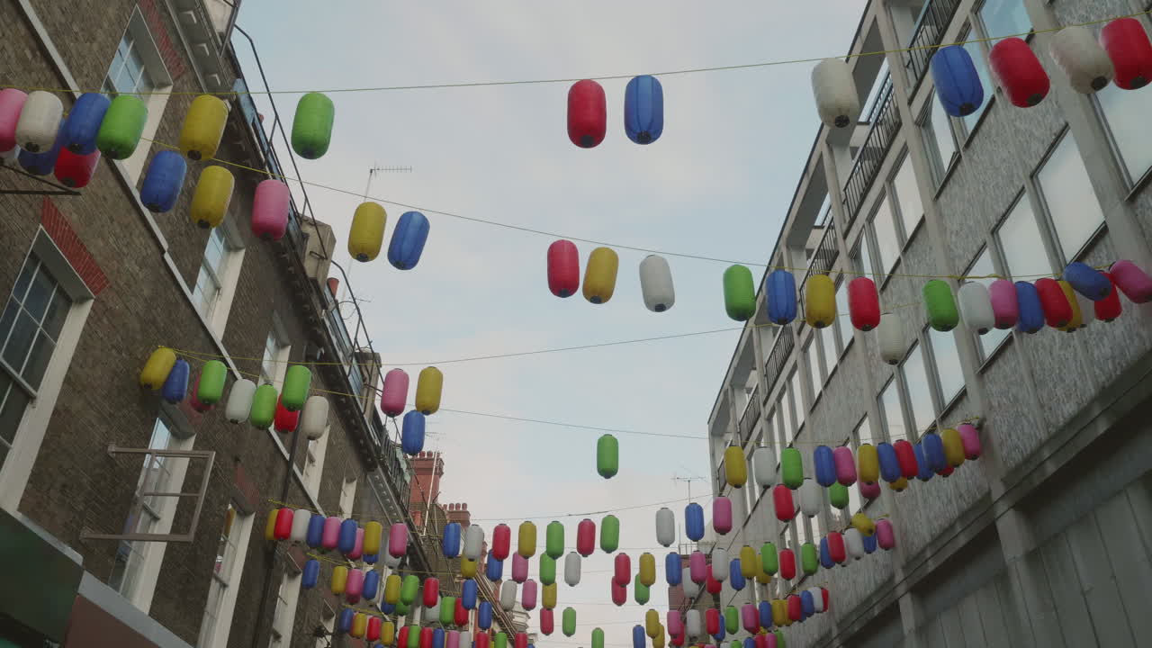 Smooth walking shot of Chinese lamps hanging between houses and dangling in the wind in Chinatown, London.