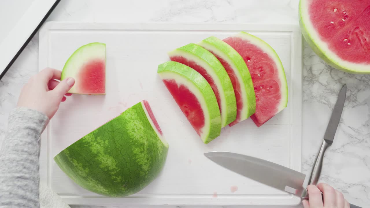 cortar la sandía roja en pedazos pequeños en una tabla de cortar blanca.