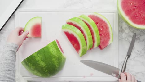 slicing red watermelon into small pieces on a white cutting board.