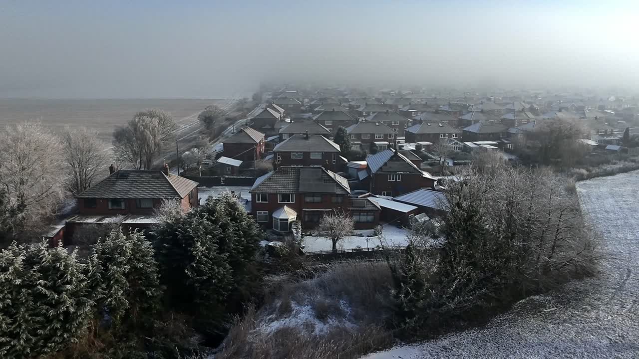 Aerial view across small town houses in England with frosty morning fog on the horizon
