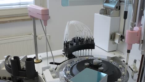 static shot of a robotic arm with needles on a modern looking medical analyzer for blood samples in a small laboratory with a window