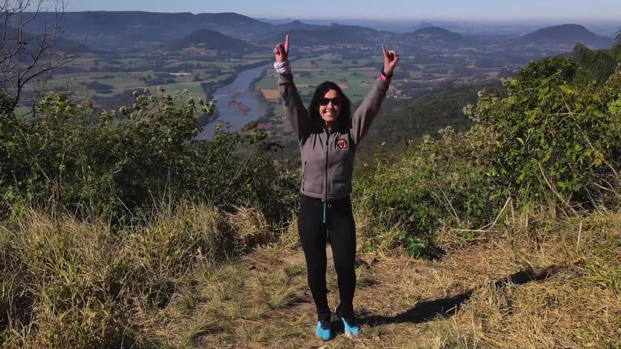 Ripresa aerea di un'escursionista che celebra l'arrivo in cima alla collina con uno splendido paesaggio con fiume e campi coltivati, con effetto dolly zoom