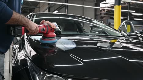 Person-polishing-black-vehicle-inside-modern-garage,-close-up-motion-shot