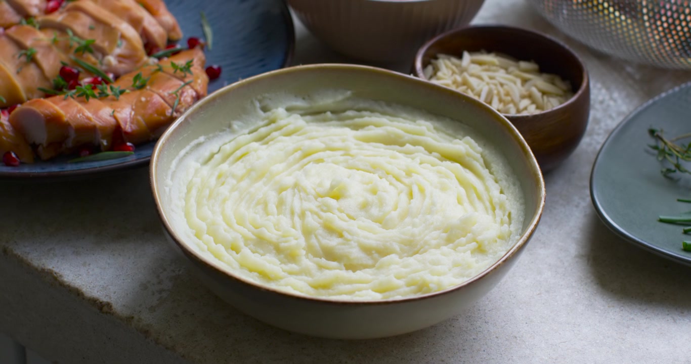 La telecamera si sposta lentamente verso l'esterno dopo l'inizio della clip, rivelando purè di patate ed erbe aromatiche pronte per essere servite.
