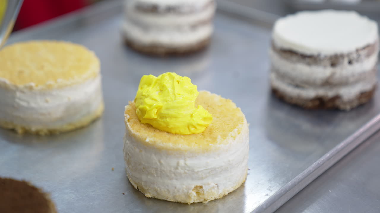 Little vanilla sponge cake is covered with bright yellow butter cream. Desserts decoration at modern food factory. Close up.