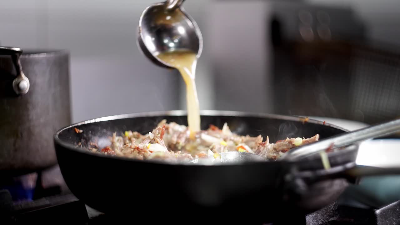 Close up view in slow motion of a Metal spoon pouring beef stock in a pan with a smoky stew.
