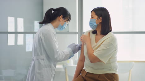female doctor vaccinating asian woman in clinic