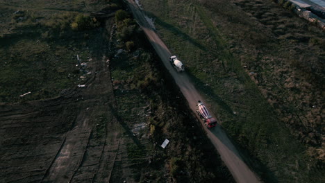 Aerial-static-shot-of-two-cement-mixer-trucks-meeting-on-a-dusty-road-4K