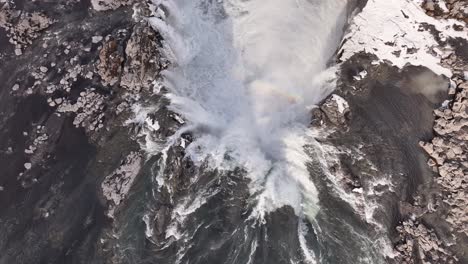 raging water flows from the volcanic cliffs of selfoss, iceland, over rocks and snow