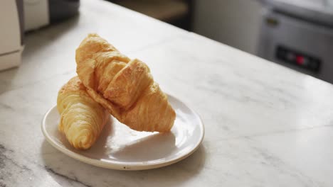 Close-up-of-two-croissants-on-white-plate-on-countertop-at-cafe