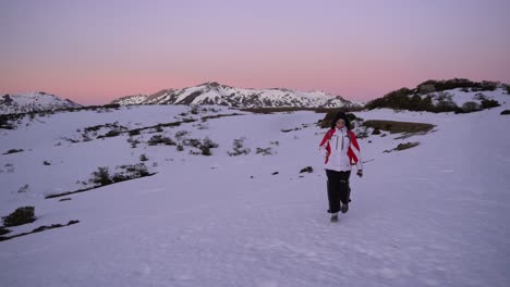toma en cámara lenta de una mujer caminando en la nieve con una hermosa puesta de sol detrás