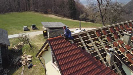 ein dachbauer auf dem dach eines hauses legt fliesen auf einem unfertigen dach, während bretter und baumaterialien im hof unten sind