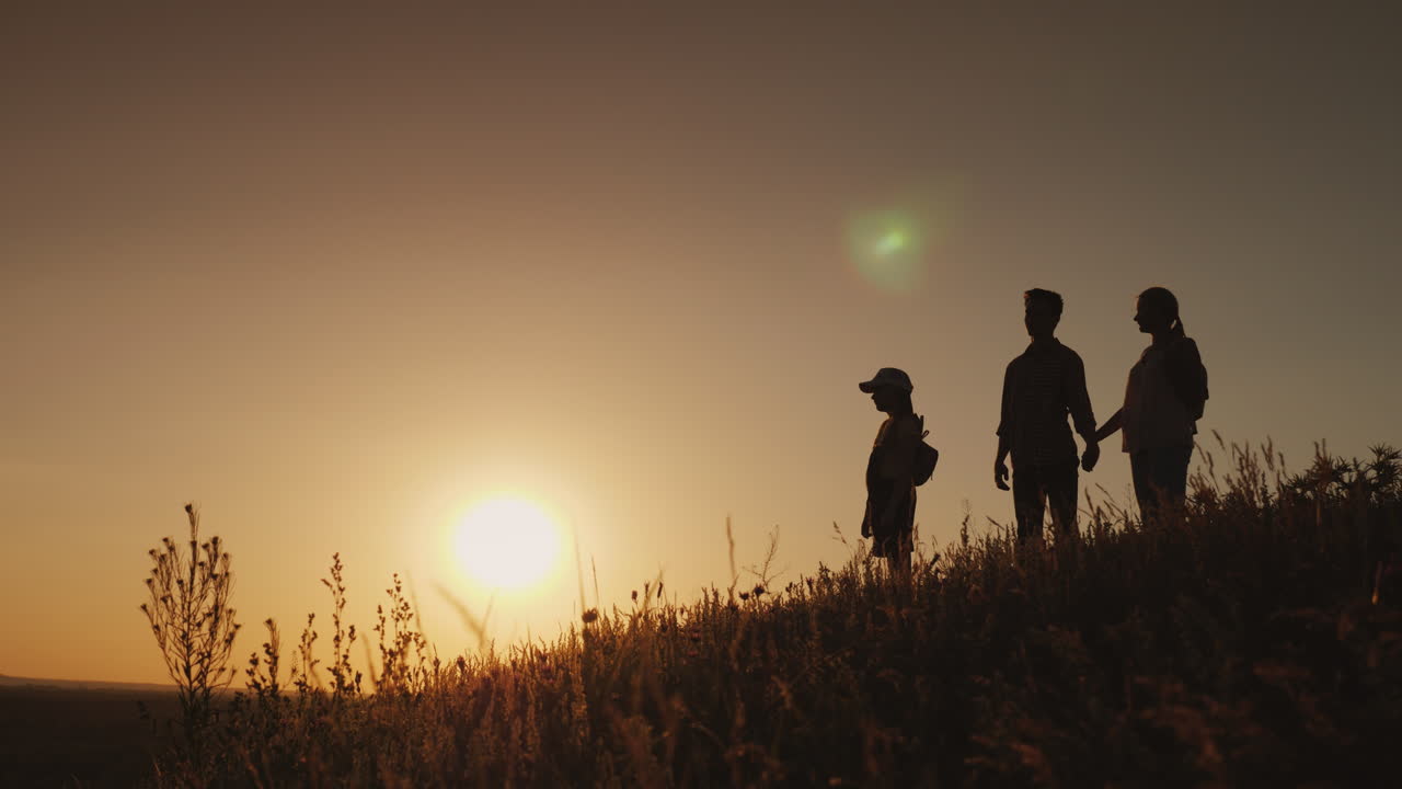 Sagome di una famiglia felice insieme. Incontrano l'alba in un luogo pittoresco. Video 4K.