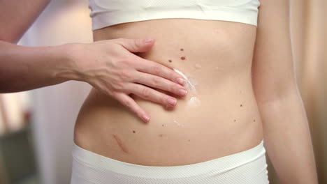 mujer aplicando con la mano crema corporal en el abdomen