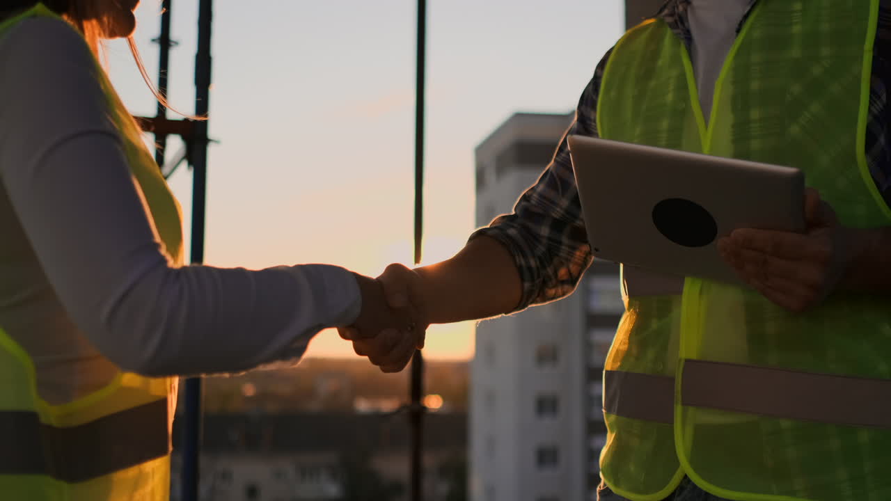 Slow motion of two engineers are talking about the future project for the construction of a skyscraper business center and shaking hands at sunset.