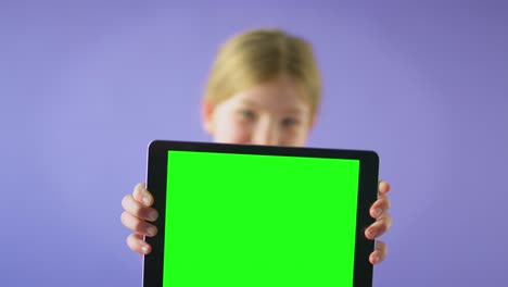 studio shot of smiling girl holding digital tablet with green screen looking at camera against purple studio background - shot in slow motion