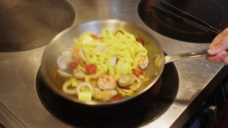 chef adding butter in a pan with tagliatelle spaghetti with seafood, professional restaurant kitchen italian mediterranean traditional pasta food close up preparation