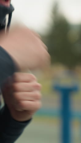 close-up of a person jogging while wearing a black jacket, with clenched fists, with a blur view of someone passing with the background blur