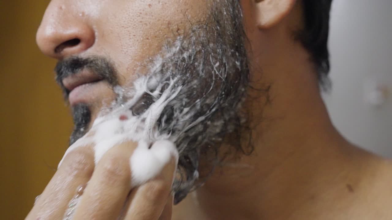 A close-up of a man with a beard gently washing it with soap, focusing on his hands and beard as the lather creates a clean, soft texture