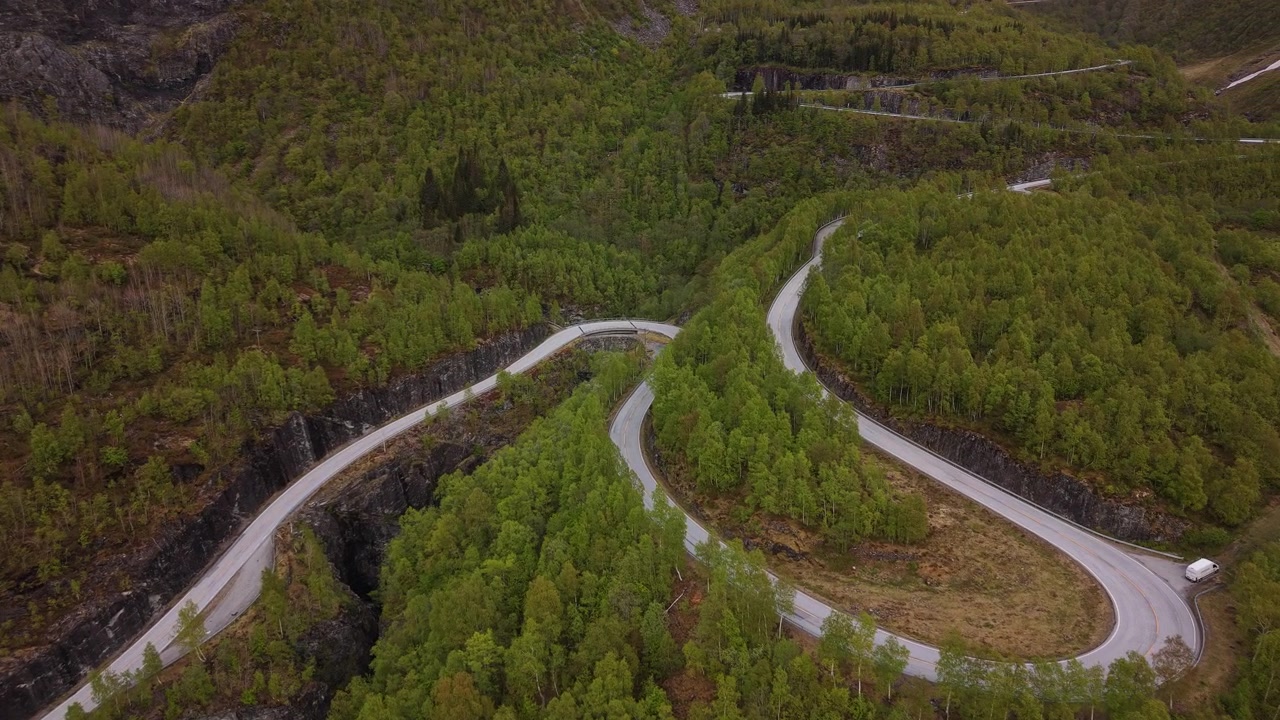 Klikatá horská silnice protíná hustý zelený les a ukazuje složité křivky krajiny. Ideální pro cestopisné dokumenty nebo vizuály z malebných road tripů.