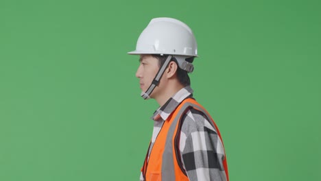 vista lateral de cerca ingeniero masculino asiático con casco de seguridad y caminando en el estudio de fondo de pantalla verde