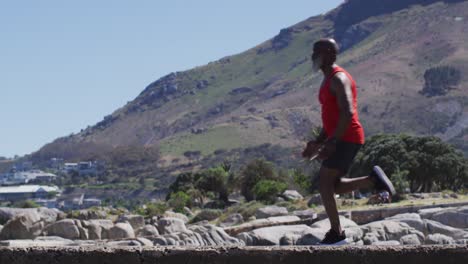 hombre afroamericano senior haciendo ejercicio corriendo sobre rocas junto al mar