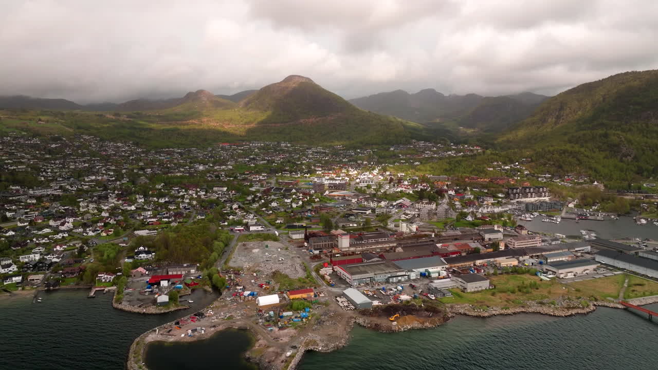 Drone panoramic pullback above Jorpeland steel mill with smokestacks and buildings near Norwegian fjord