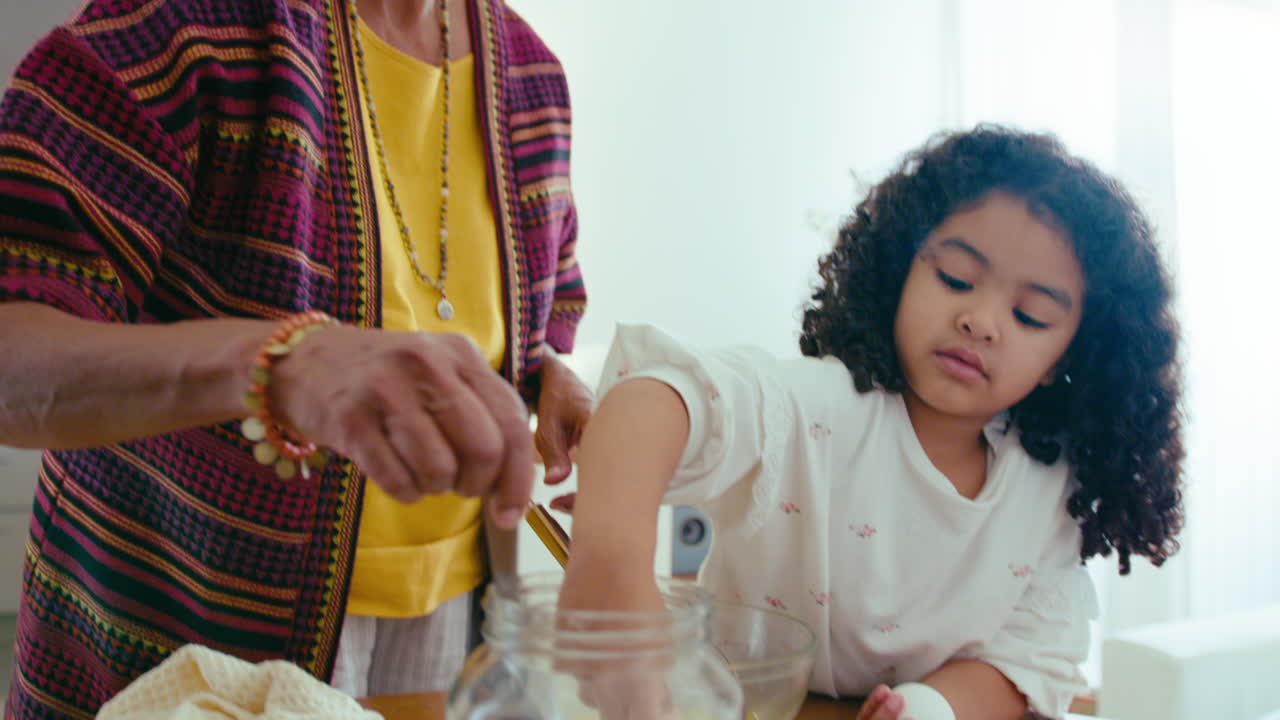 작은 흑인 소녀가 할머니가 집에서 요리하는 것을 도와줍니다.