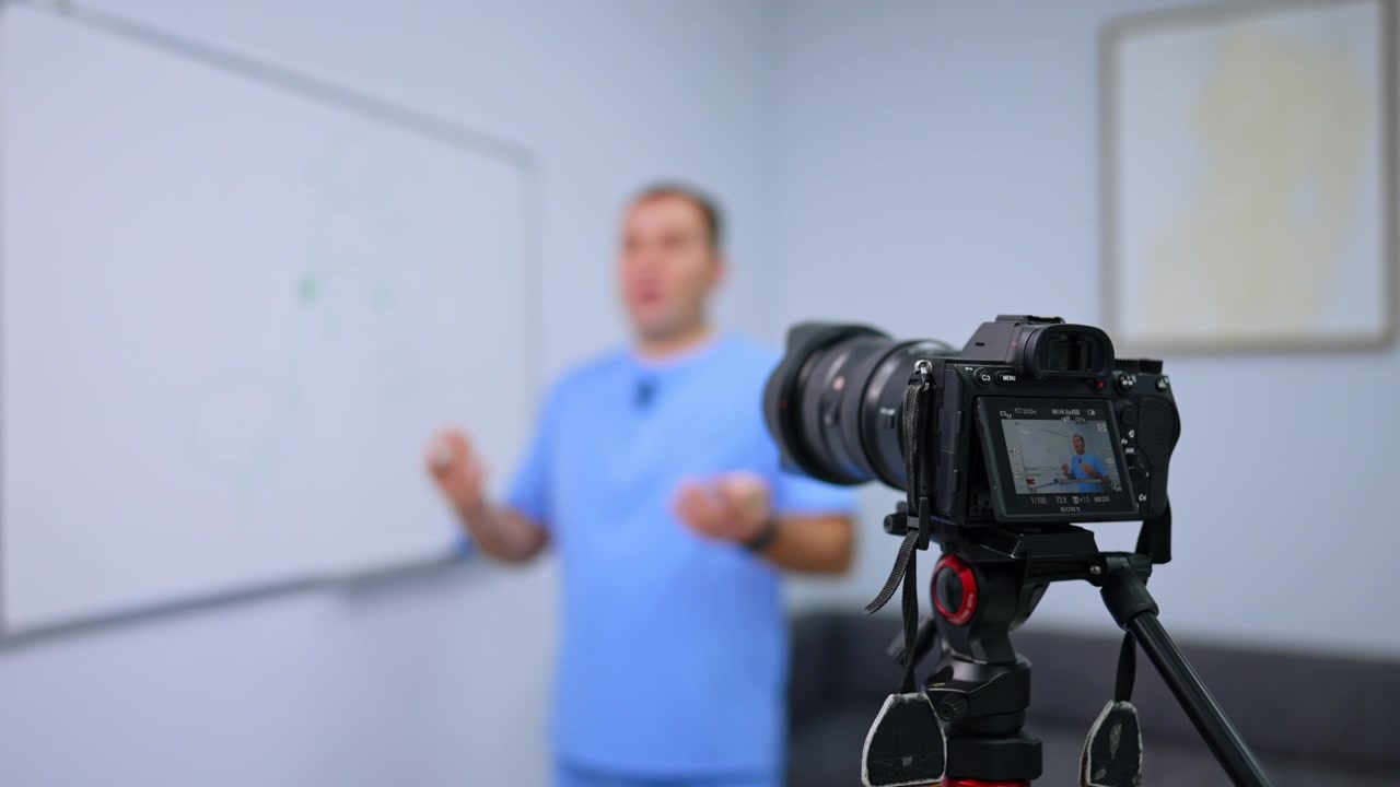 Kiev, Ucrânia, 9 de agosto de 2026: Câmera filmando uma aula de saúde ao lado de um quadro branco. Um tripé e um monitor traseiro permanecem em foco enquanto um homem de uniforme azul gesticula ao fundo