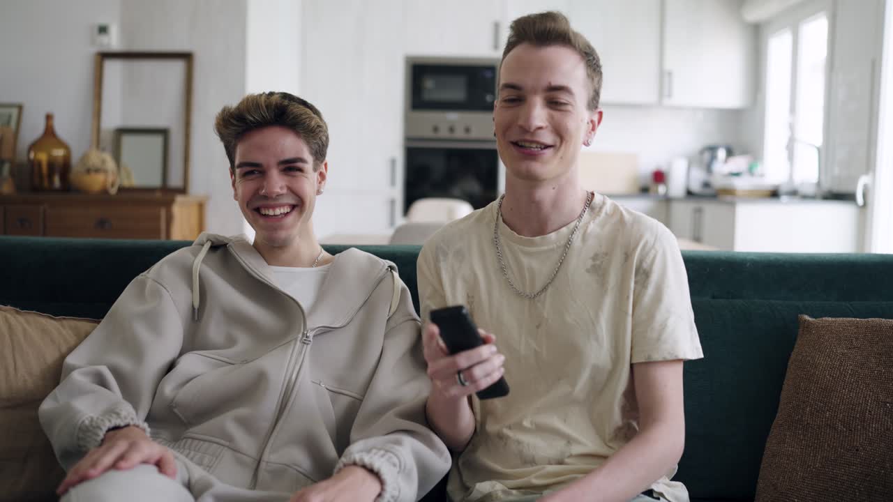 To unge mænd griner, mens de ser tv på sofaen