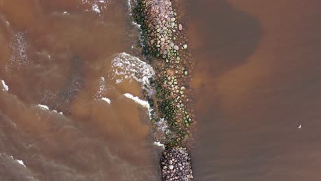 Sea-waves-hitting-mole-covered-with-stones-in-top-down-aerial-view