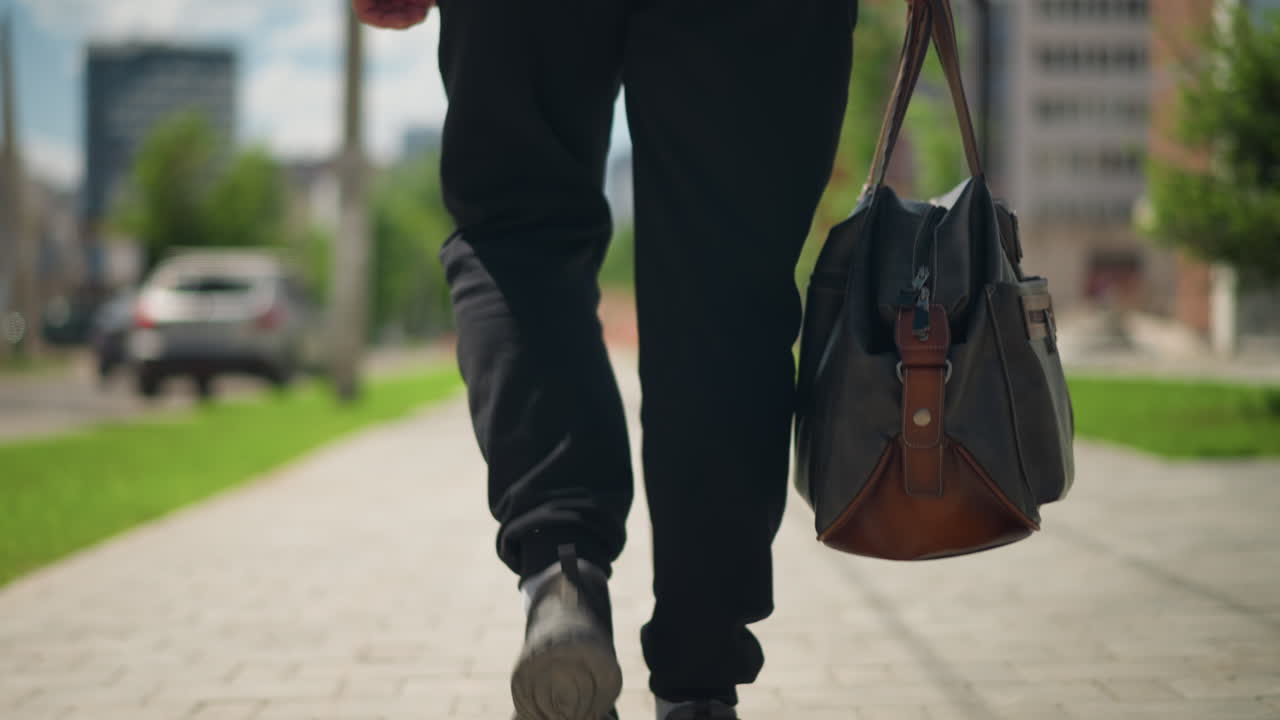 un hombre camina con determinación en un entorno urbano; una persona avanza con determinación por la acera, un peatón con una bolsa de lona camina sobre adoquines con un fondo urbano difuminado