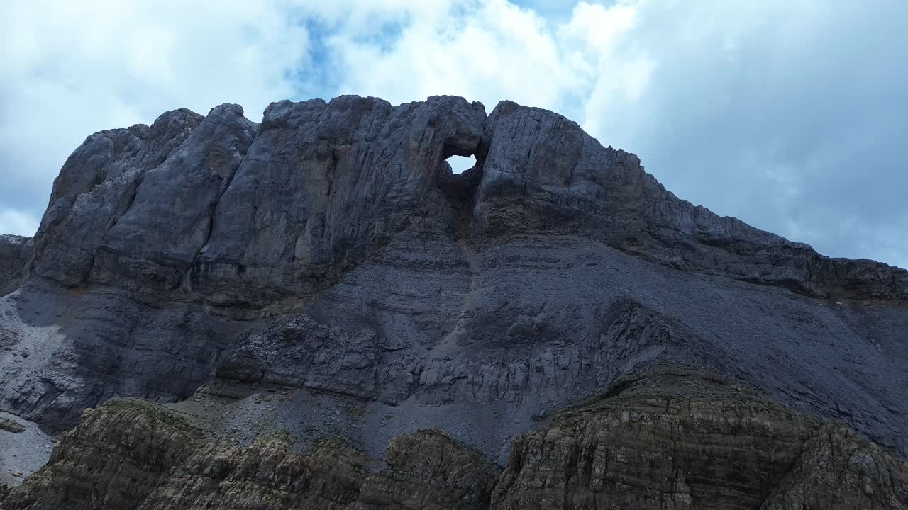 Aerial zoom in on the dramatic rocky mountain with a natural arch, under a cloudy sky in Valle de Ip, Aragon