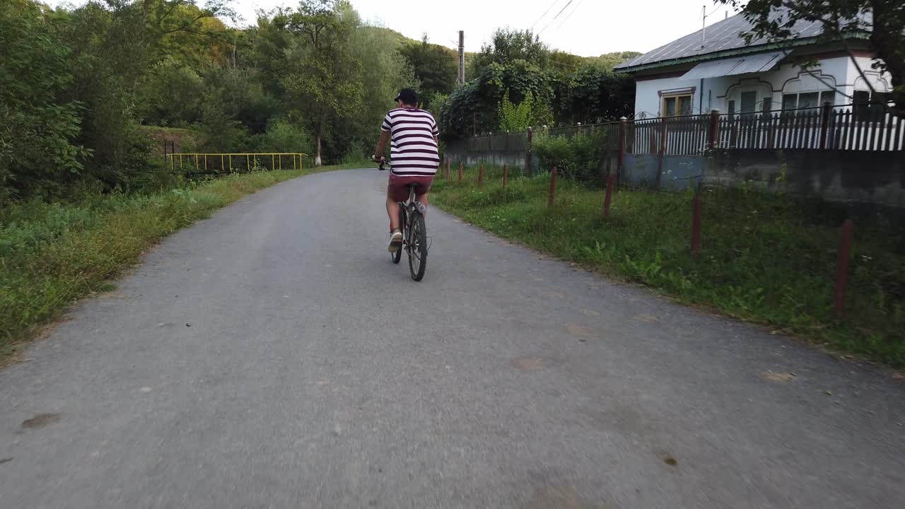 Close up shot of male cyclist filmed from behind on a country road. Man in casual summer clothes riding bike , shot from behind