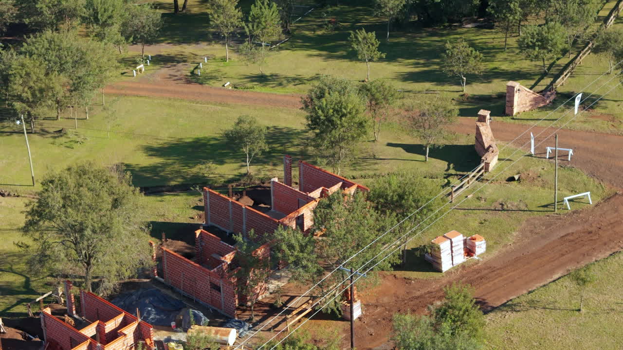Backward movement drone footage going over rural condominium construction site near jungle edge during afternoon, with vast vegetation.