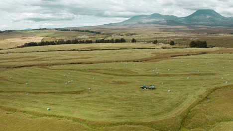 tractor creating hay bales on rural green grass field, agriculture concept, new zealand countryside landscape, aerial