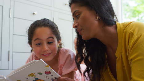 Cerca-De-Madre-E-Hija-En-Casa-Tumbadas-En-El-Suelo-En-El-Salón-Leyendo-Un-Libro-Juntas