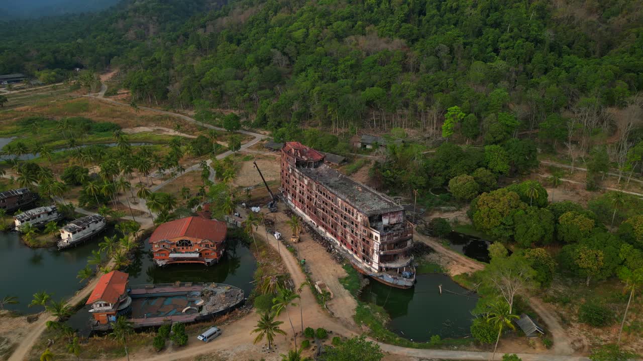 abandoned rusty ghost ship on Koh Chang on tropics island bay, Thailand, during sunset, with a crane working on it. Perfect aerial view flight drone camera pointing down