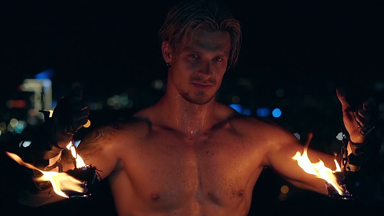 젊은 금발 남성이 두 개의 불타는 독을 내려 놓고 체인에 매달려 느린 동작 촬영 클로즈업 촬영