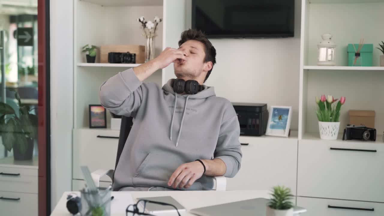 The charismatic young man, a rapper, sits behind a table in the studio and passionately performs rap into the camera, gesturing with his hands.