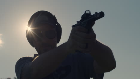 man firing pistol in silhouette with sunburst
