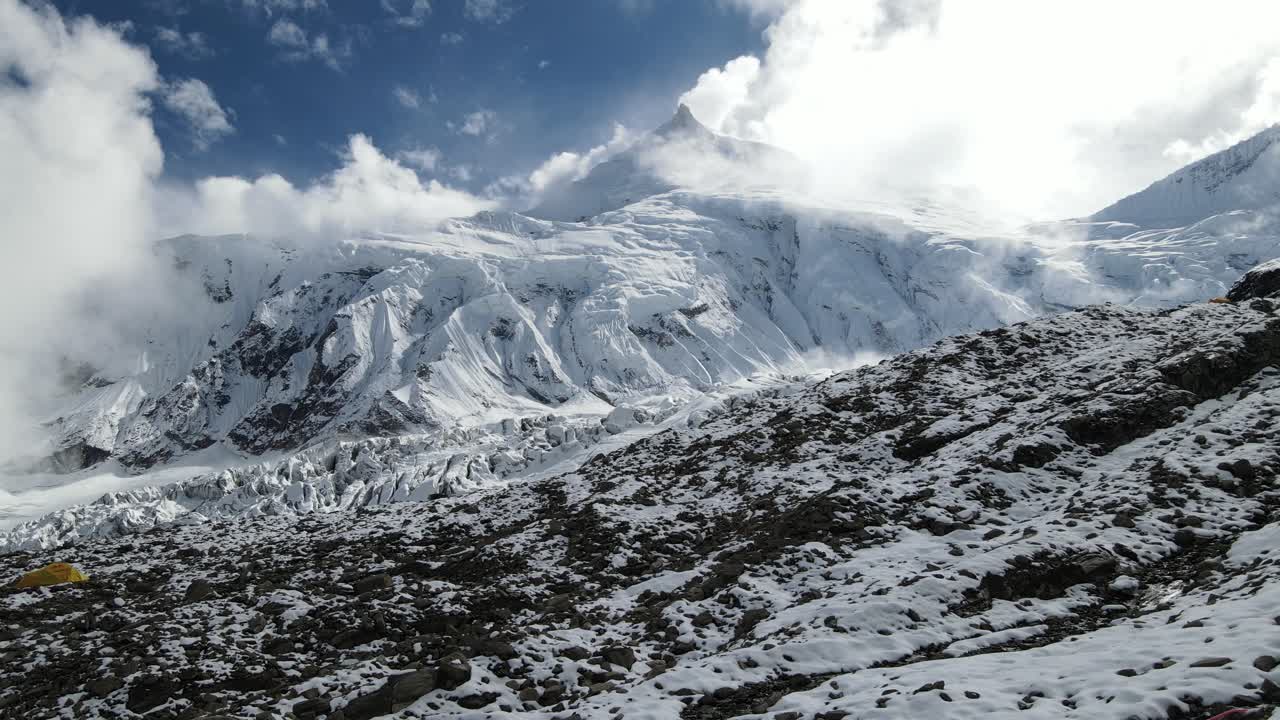 Drone footage showcases Manaslu Base Camp below the 8,163m Himalayan peak. The scene reveals snowy ridges, rugged terrain, and the dramatic high-altitude environment of this remote mountain region